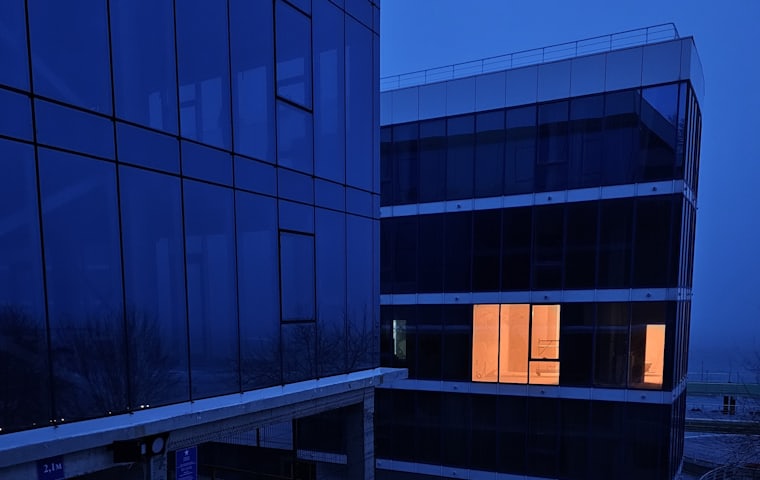 Glass-fronted corporate offices at dusk with a single lit window
